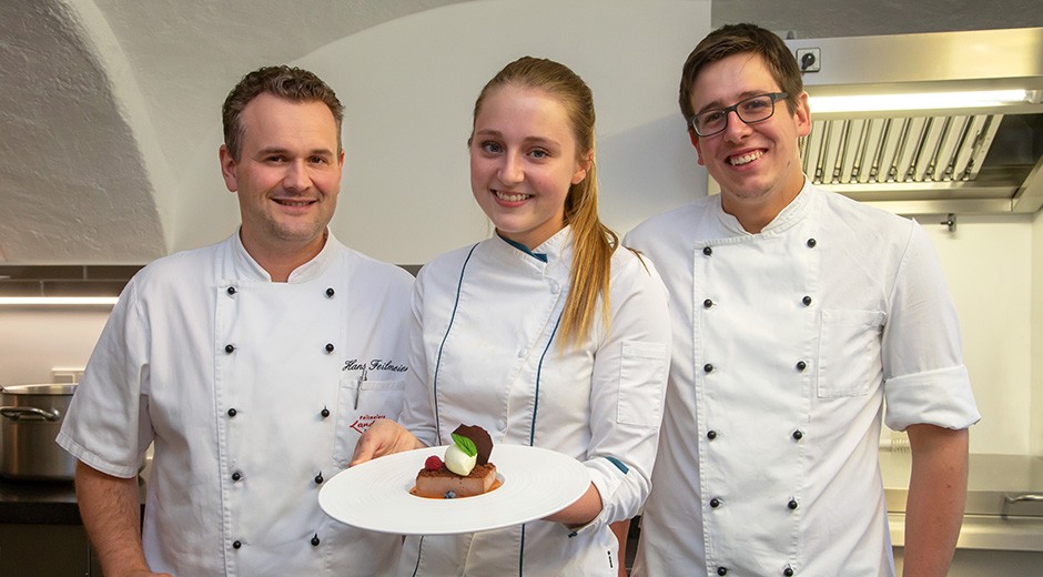 Eva (1. Lehrjahr) und Benedikt (2. Lehrjahr) haben ihre Ausbildung bei Küchenmeister Hans Feilmeier (links) bereits begonnen. Bis November werden noch drei weitere Auszubildende hinzukommen.